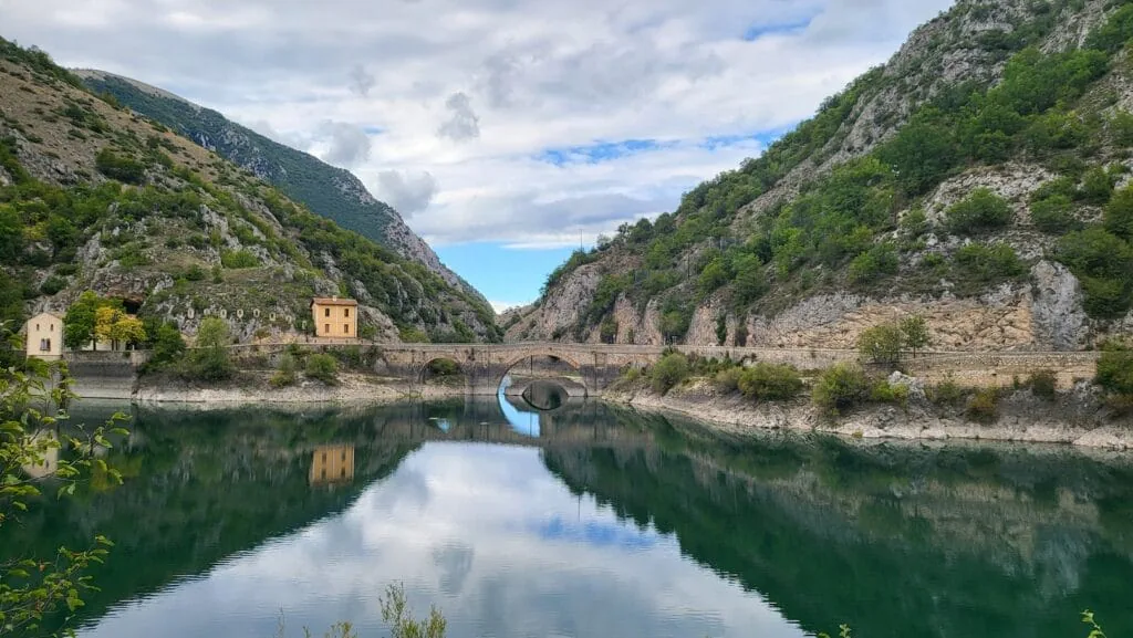 Mountain lake in Abruzzo mirroring a stone arch bridge and hillside stone buildings