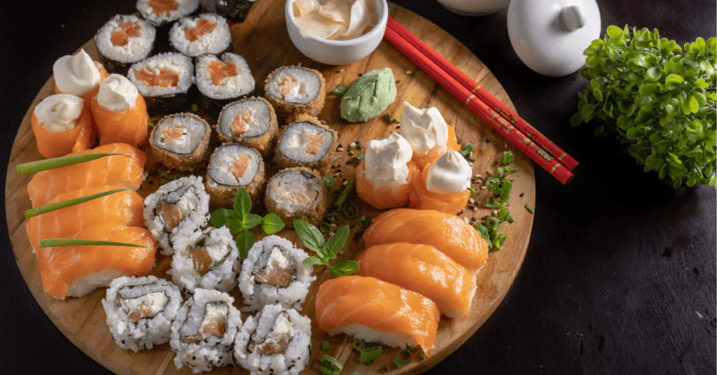 Wooden board of assorted sushi rolls and salmon nigiri with wasabi and red chopsticks