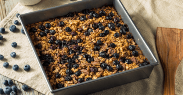 Baked blueberry oatmeal in a square metal pan with fresh blueberries scattered alongside
