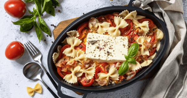 Baked feta pasta with farfalle, roasted tomatoes and a block of feta topped with basil