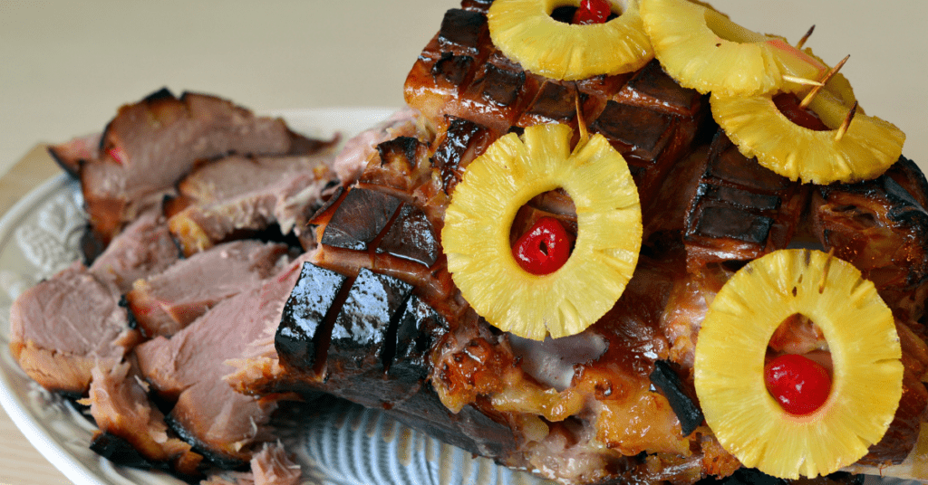 Sliced glazed baked ham studded with pineapple rings and maraschino cherries on a platter