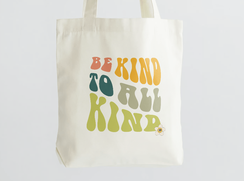 Natural canvas tote bag printed with retro lettering reading "Be kind to all kind"