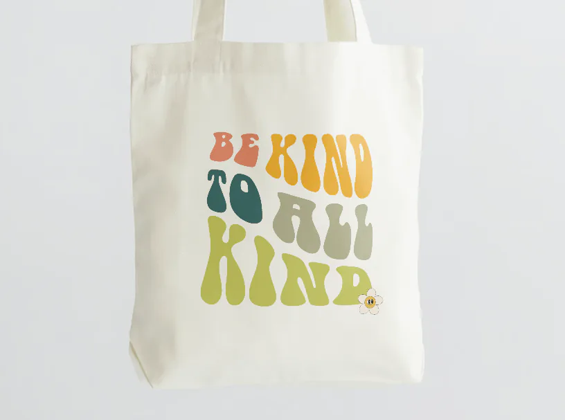 Natural canvas tote bag printed with retro lettering reading "Be kind to all kind"
