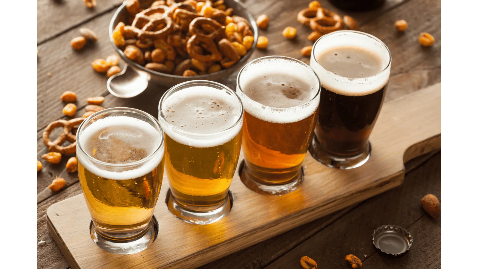 Flight of four beers from pale lager to dark stout on a wooden paddle with pretzels