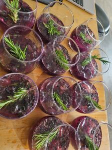 Glasses of purple berry cocktail on a wooden board, each garnished with a sprig of rosemary