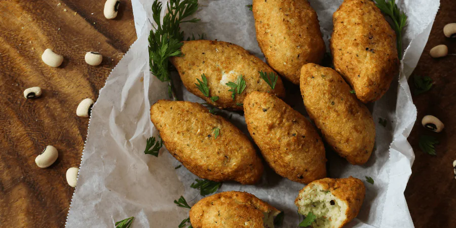 Golden black-eyed pea fritters on parchment paper with fresh herbs and scattered beans