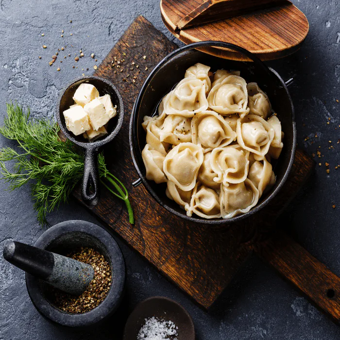 Pot of steamed dumplings with butter, fresh dill and a mortar of cracked pepper