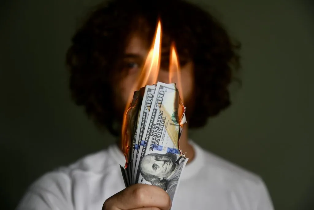 Person holding a burning hundred dollar bill up in front of their face