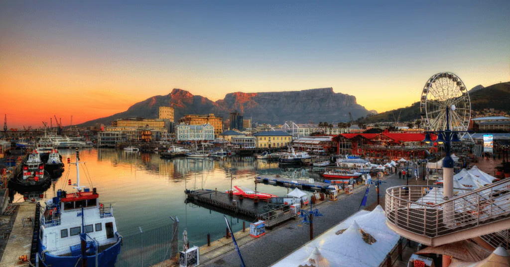 Cape Town’s harbour at sunset with Table Mountain, a Ferris wheel and moored fishing boats
