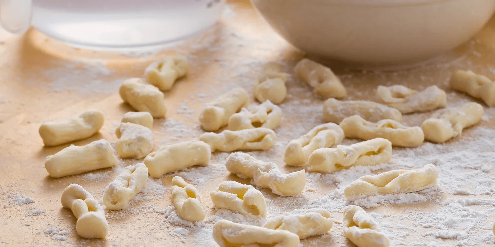 Hand-rolled cavatelli pasta scattered on a floured surface beside a white mixing bowl
