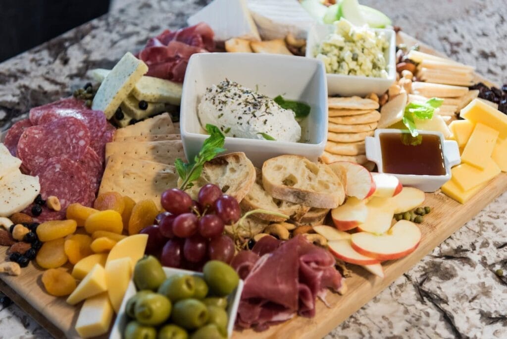 Charcuterie board with burrata, salami, prosciutto, olives, apple slices, crackers and a dish of honey