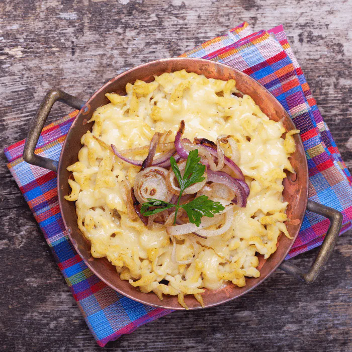 Copper pan of cheese spaetzle topped with fried onions and parsley
