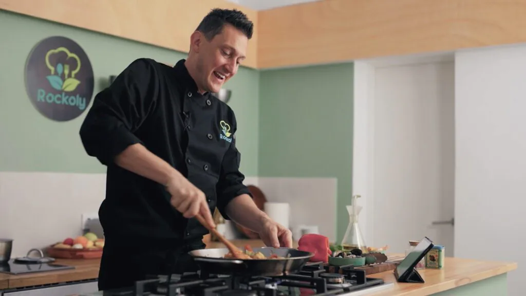 Chef stirring a pan on the stove while streaming a live online cooking class from a studio kitchen