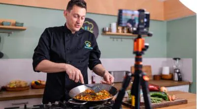Chef cooking in a skillet while a phone on a tripod films the class