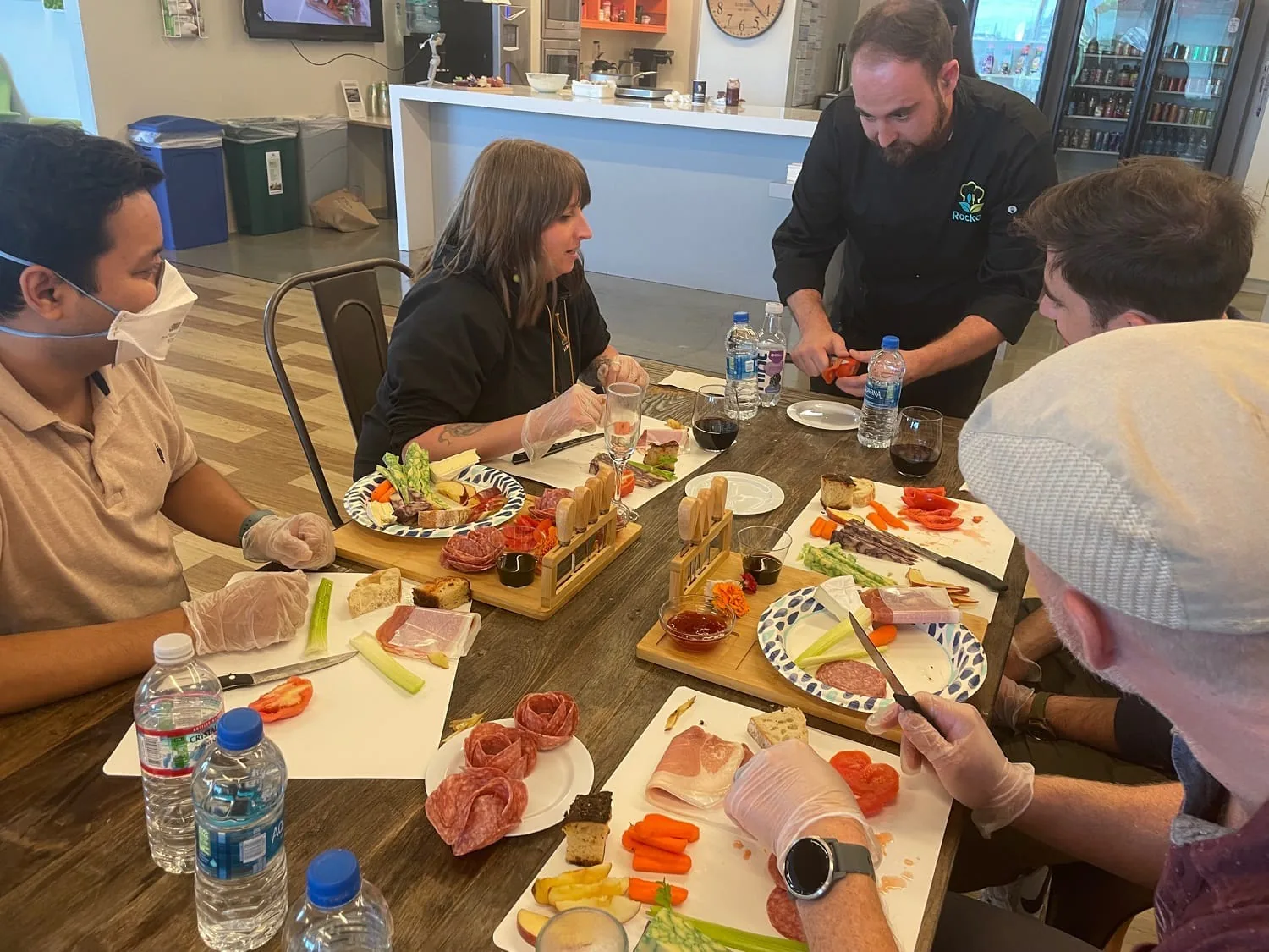 Chef leaning over a table guiding participants as they build charcuterie boards with meats and vegetables