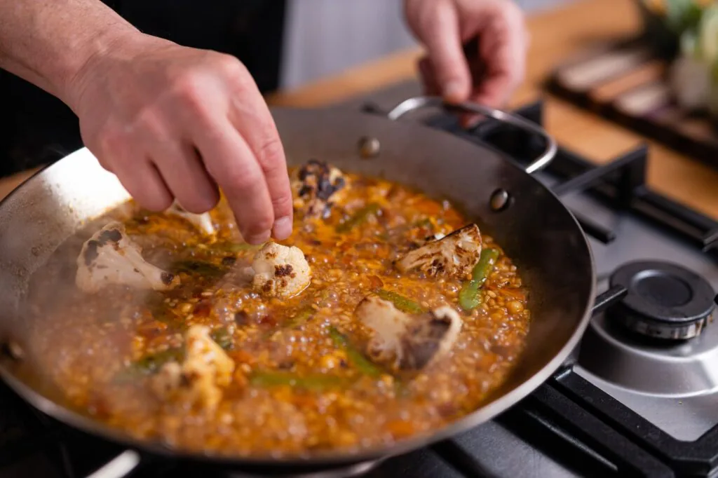 Chef Josh adding chicken to a bubbling paella of rice, green beans and saffron broth on the stove