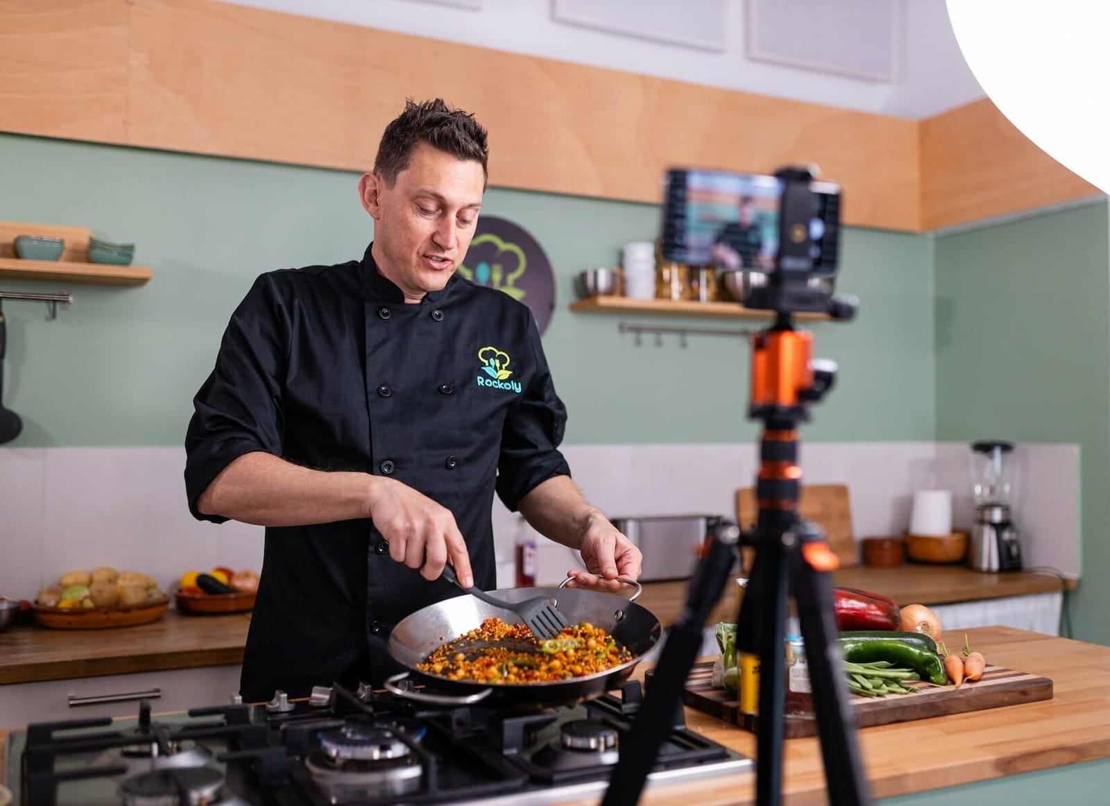 Chef Josh cooking paella on a gas range while a phone on a tripod films the demo