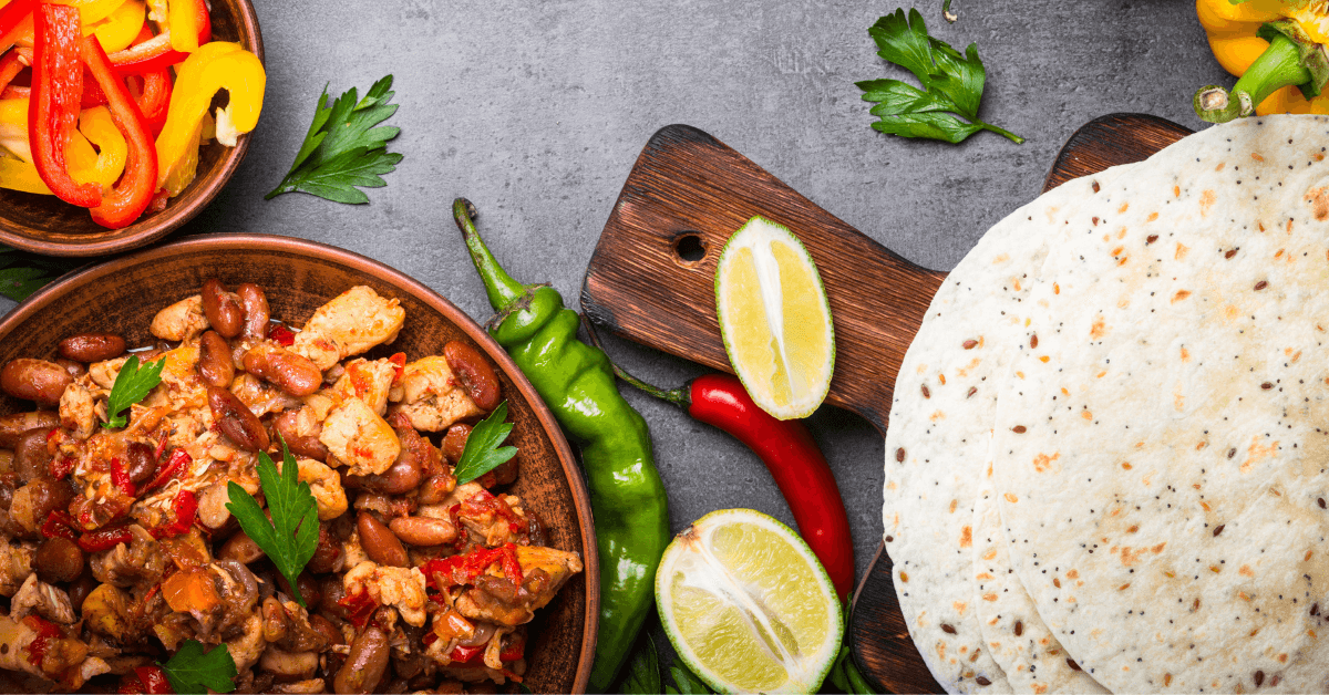 Bowl of chicken and bean stew with peppers, served with flour tortillas, lime and green chiles