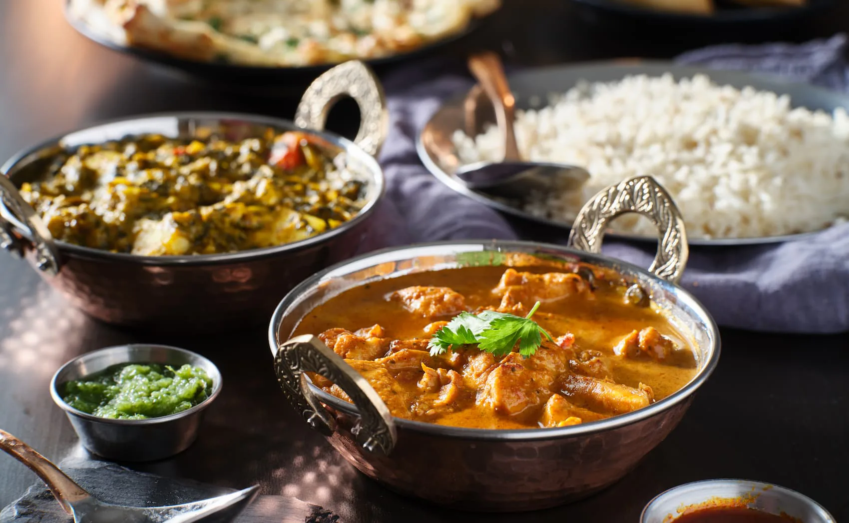 Copper bowls of chicken curry and saag paneer served with basmati rice, naan and green chutney