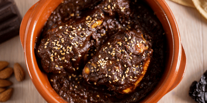 Seared chicken topped with dark pipián mole sauce in a clay pot