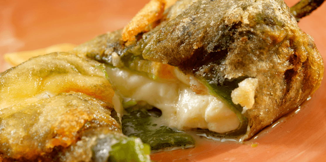 Battered chile relleno split open with melted cheese spilling onto the plate