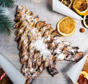 Chocolate swirl puff pastry Christmas tree dusted with powdered sugar beside dried orange slices