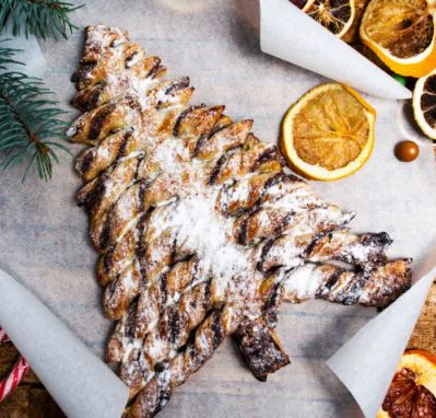 Chocolate swirl puff pastry Christmas tree dusted with powdered sugar beside dried orange slices