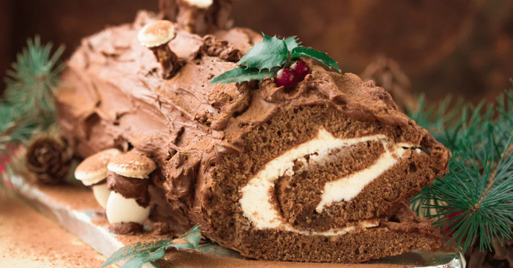 Chocolate yule log cake with a cream swirl, meringue mushrooms and holly beside pine branches