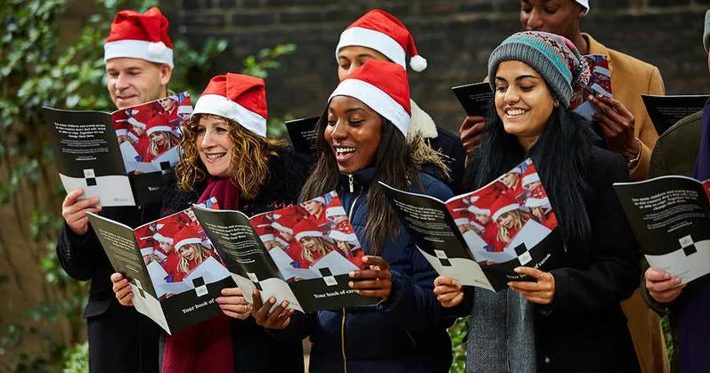 Group of carolers in Santa hats singing outdoors from song booklets