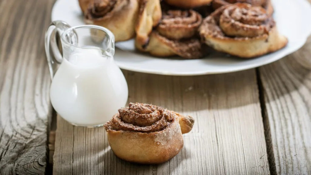 Freshly baked cinnamon rolls on a plate with a glass jug of milk on a weathered wooden table