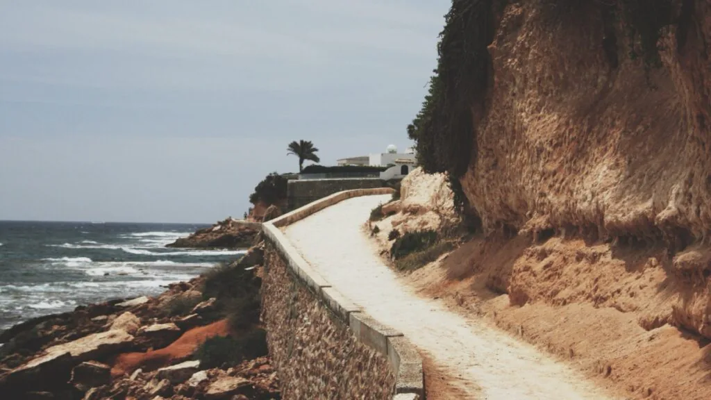 Stone walkway curving along a rocky coastline beside a choppy blue sea