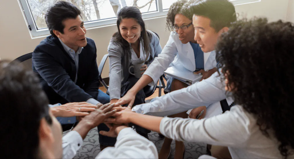 Colleagues in an office circle stacking their hands together in a team huddle