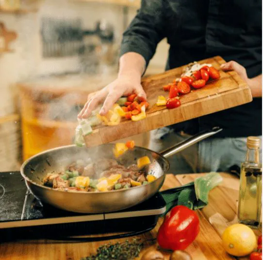 Cook tipping chopped peppers and vegetables from a wooden board into a sizzling pan