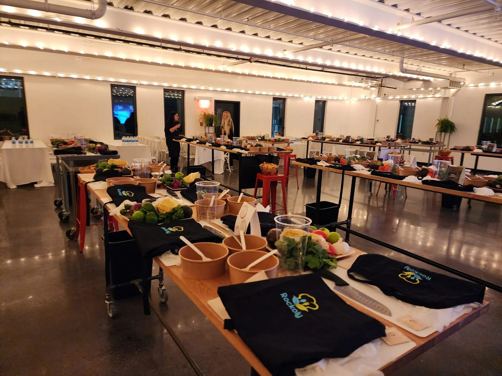 Long event hall set with rows of cooking stations, aprons, cutting boards and fresh produce