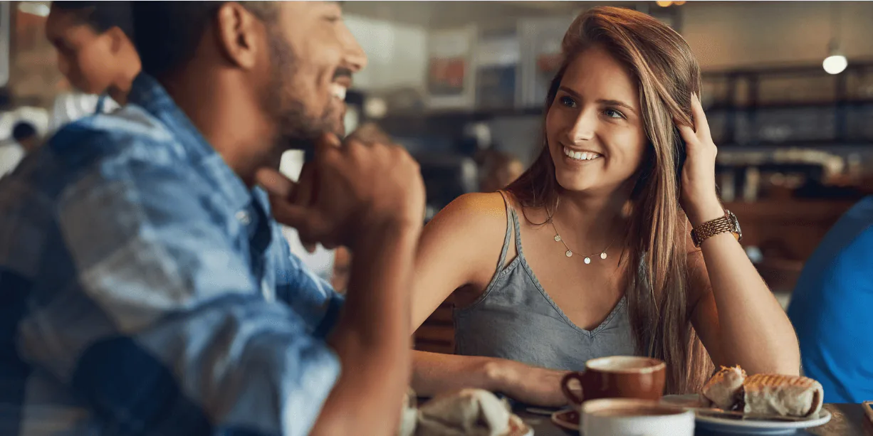 A smiling couple talking across a cafe table set with coffee cups and pastries
