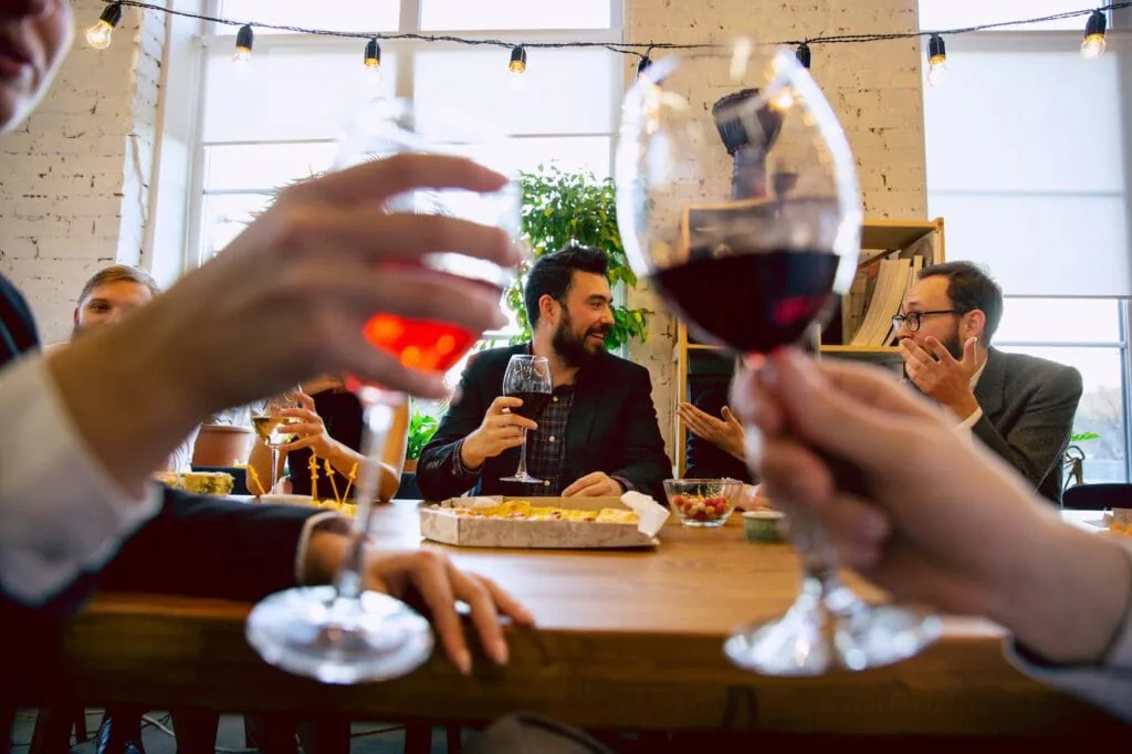 Coworkers raising glasses of red wine around a dinner table under string lights