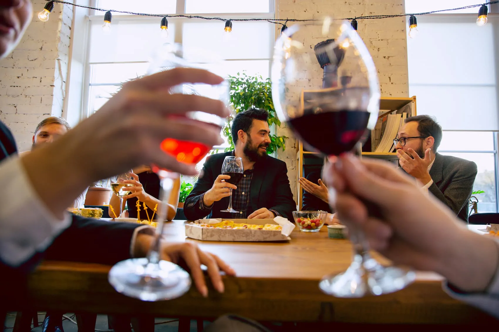 Colleagues raising glasses of red wine around a table of food under string lights