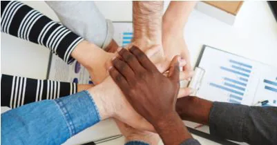 Diverse group of hands stacked together over a desk of printed charts