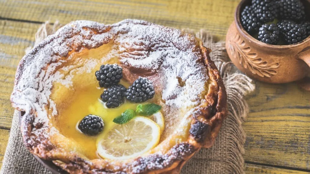 Overhead Dutch baby pancake dusted with powdered sugar, topped with blackberries, a lemon slice and mint
