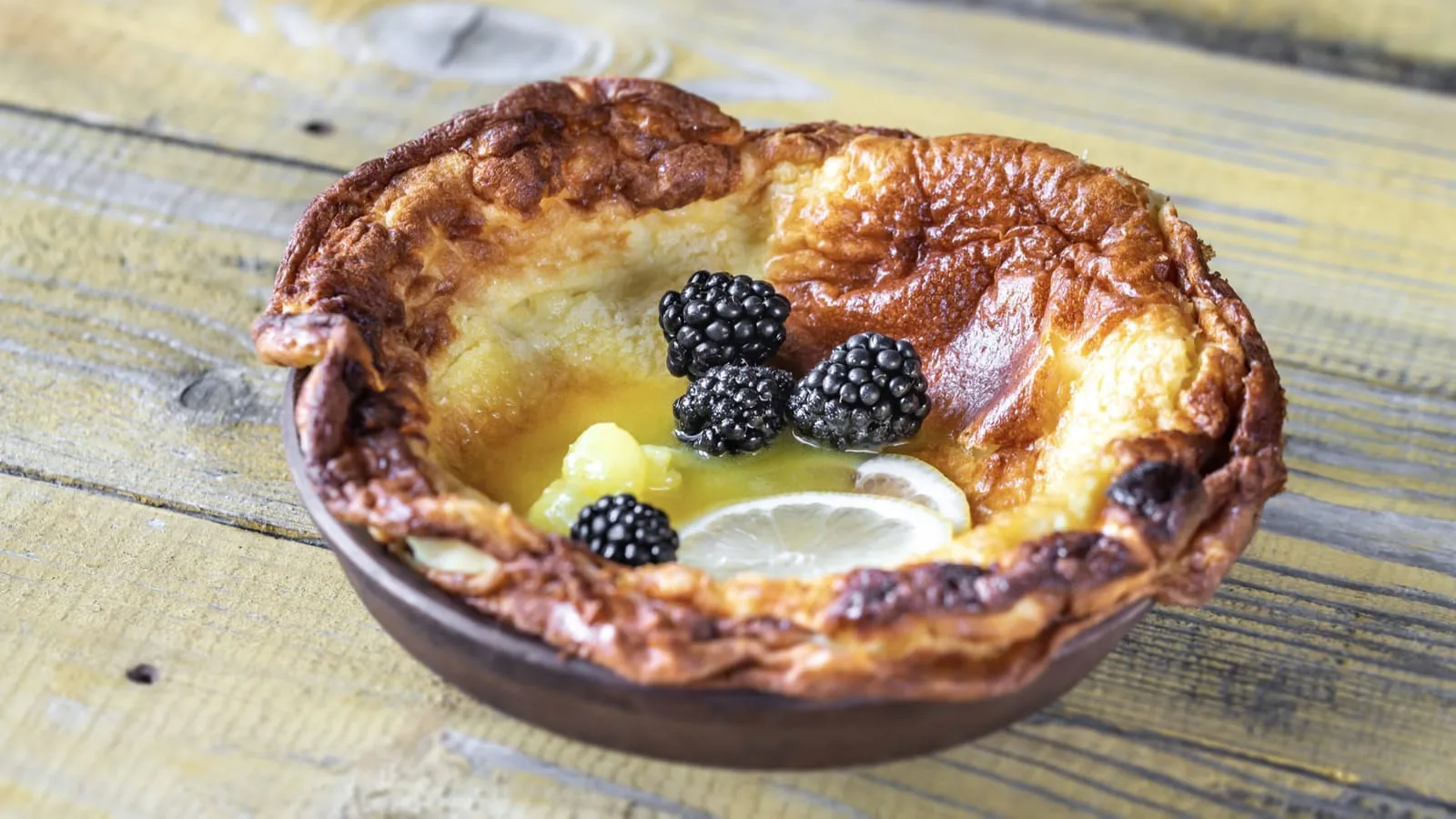 Golden baked Dutch baby pancake filled with blackberries and lemon slices in a ceramic dish