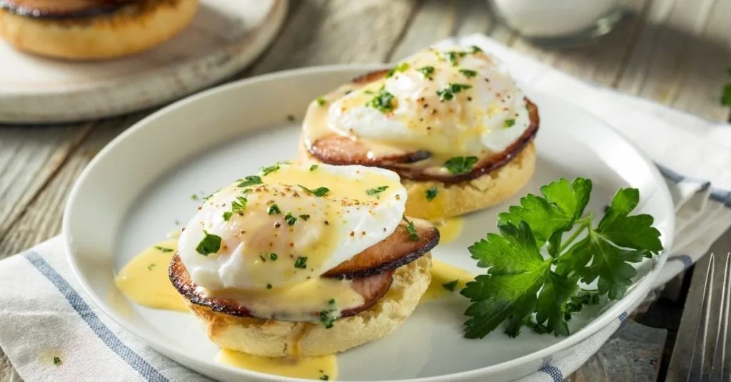 Two eggs Benedict on English muffins with Canadian bacon, hollandaise and chopped chives