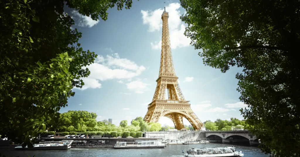 The Eiffel Tower framed by green trees above the Seine, with tour boats moored on the river