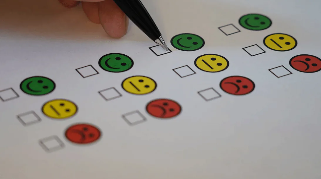 Hand with a pen filling in a survey of green, yellow and red smiley-face rating boxes