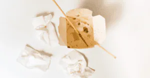 Empty cardboard takeout container with a chopstick and crumpled napkins on a white surface