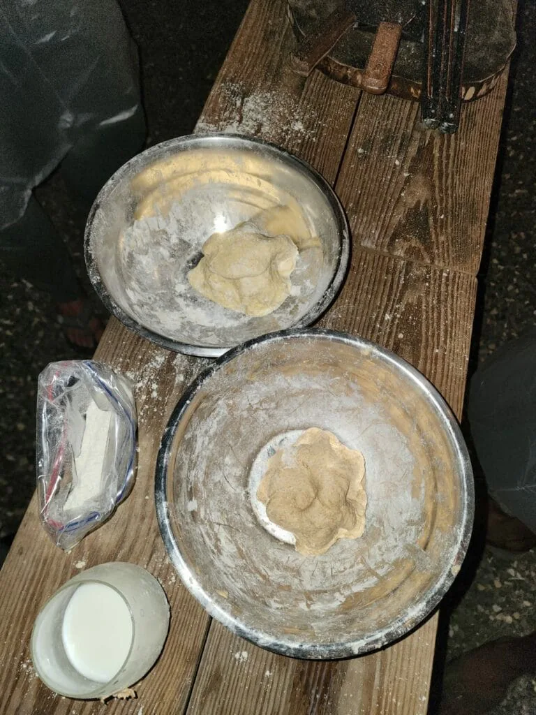 Balls of festival dough resting in flour-dusted metal bowls on a wooden table