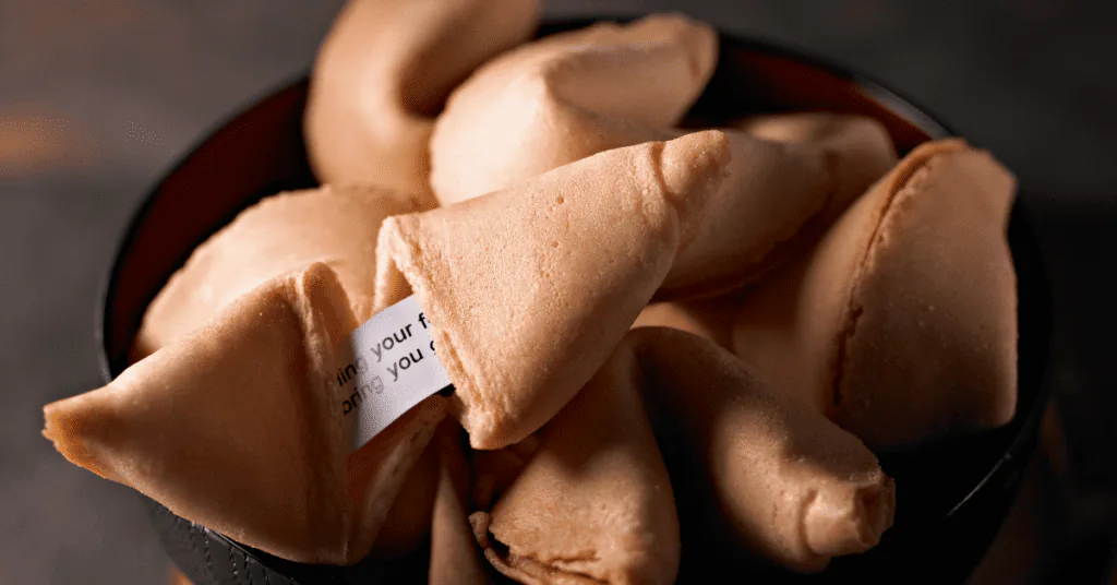 Bowl of fortune cookies with a paper fortune slipping out of one