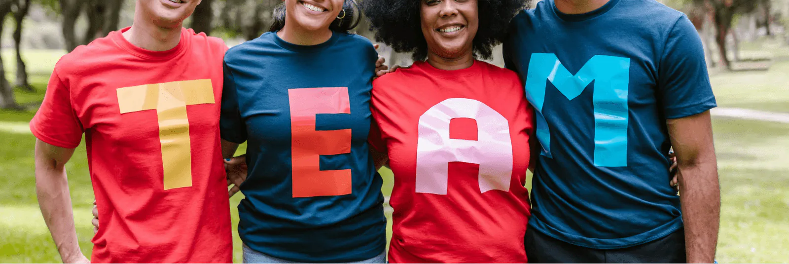 Four colleagues standing arm in arm wearing T-shirts whose letters spell out the word TEAM