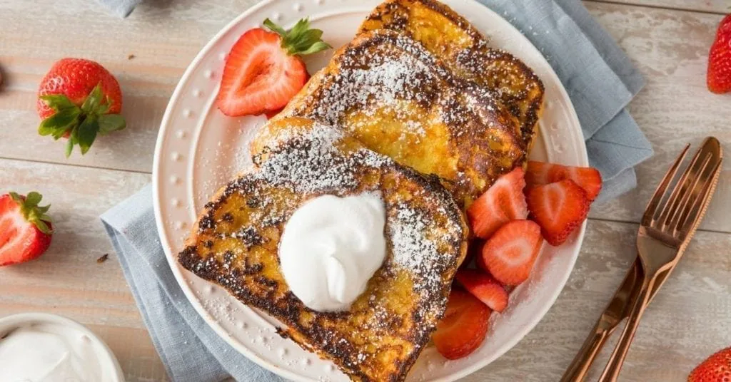 French toast dusted with powdered sugar, topped with whipped cream and fresh strawberries