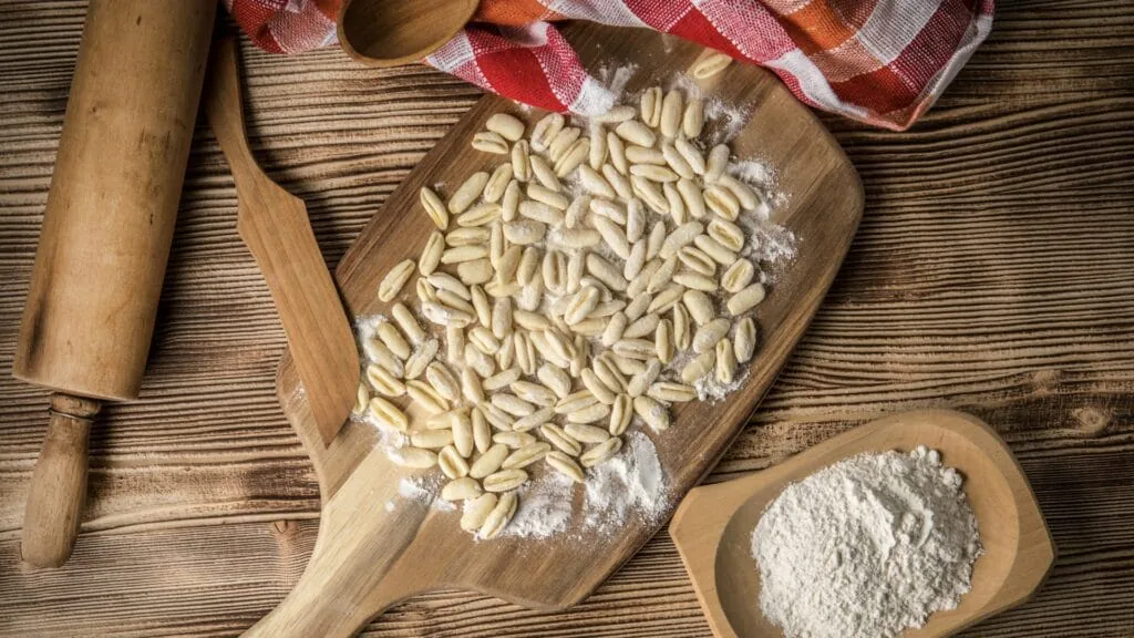 Fresh cavatelli pasta dusted with flour on a wooden board beside a rolling pin