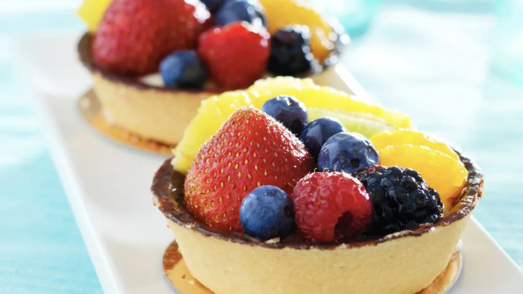 Two fruit tarts piled with strawberries, blueberries, raspberries, blackberries and orange segments